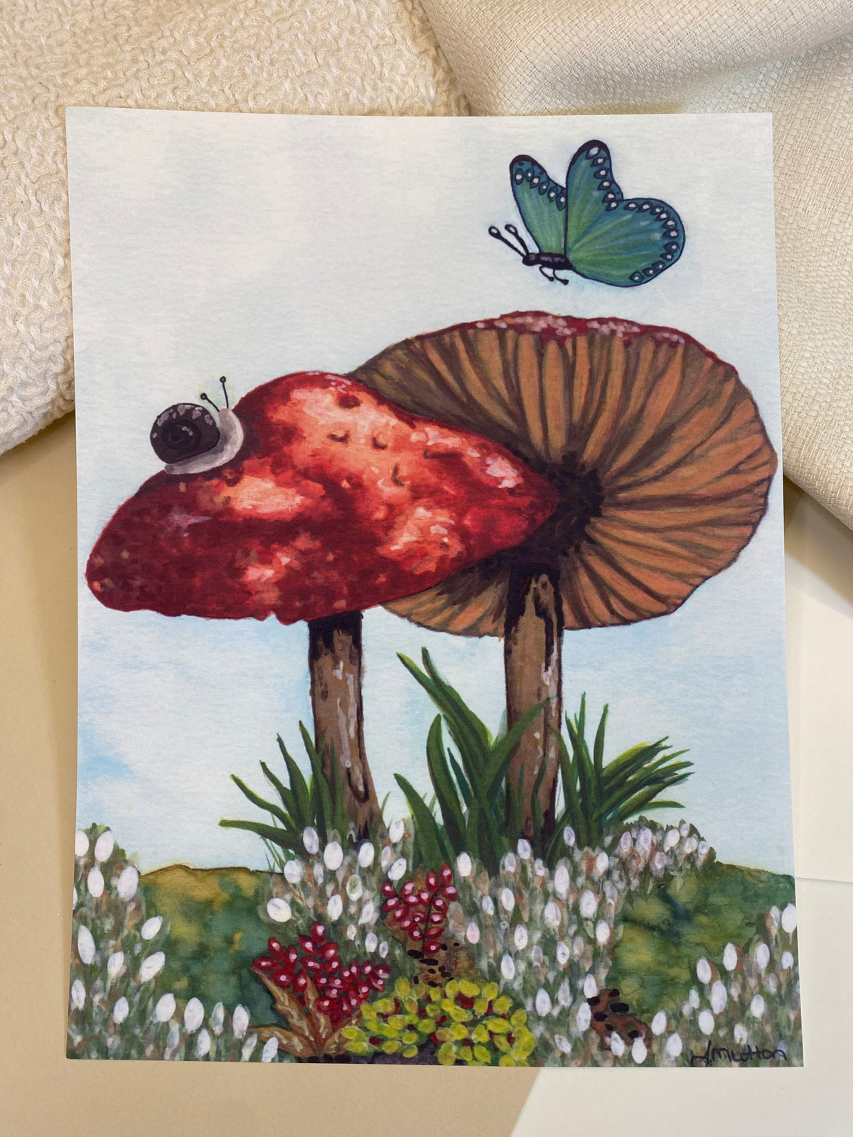 Unframed mushroom art print resting on a light surface beside cream fabric.