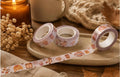 Three rolls of patterned washi tape on a ceramic tray, styled with dried flowers, a candle, and a knitted blanket in a warm autumn setting.