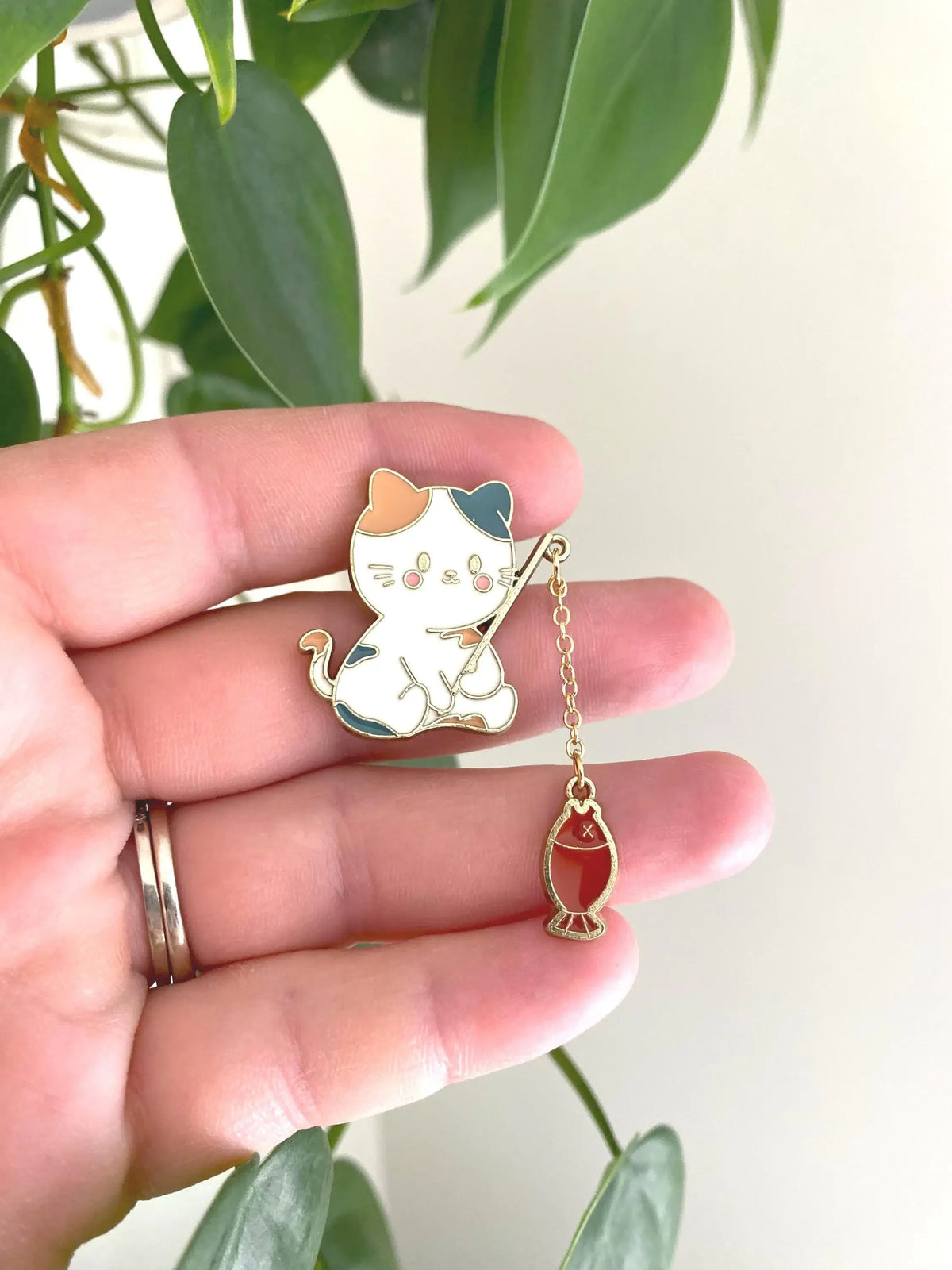 Cute Cat Fishing Enamel Pin held in a hand, featuring a kitty with a fishing rod and dangling fish charm.